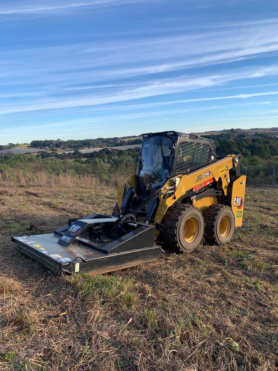 Minicarregadeira Cat 250 com roçadeira em campo aberto